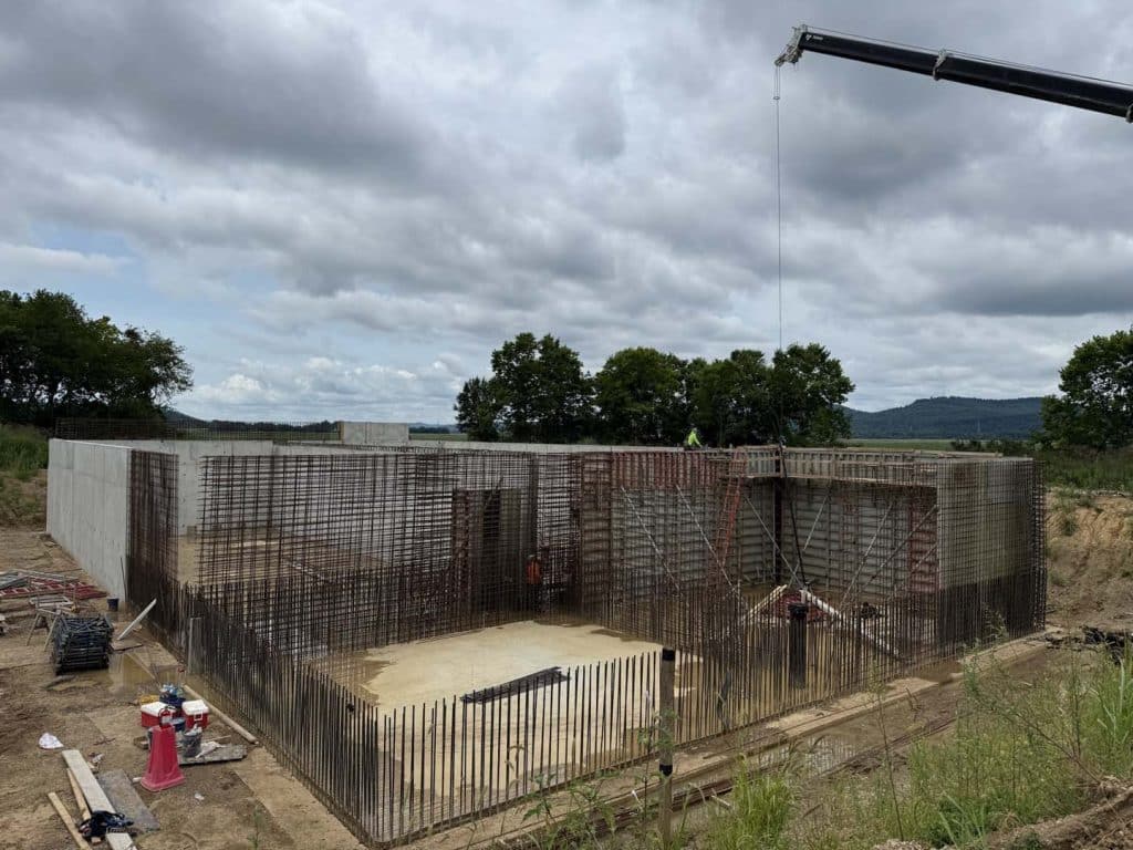 Concrete foundation under construction with exposed rebar and a crane overhead.