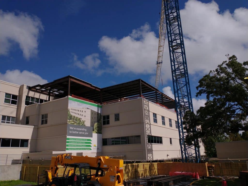 Construction crane beside a hospital building with rooftop expansion underway.