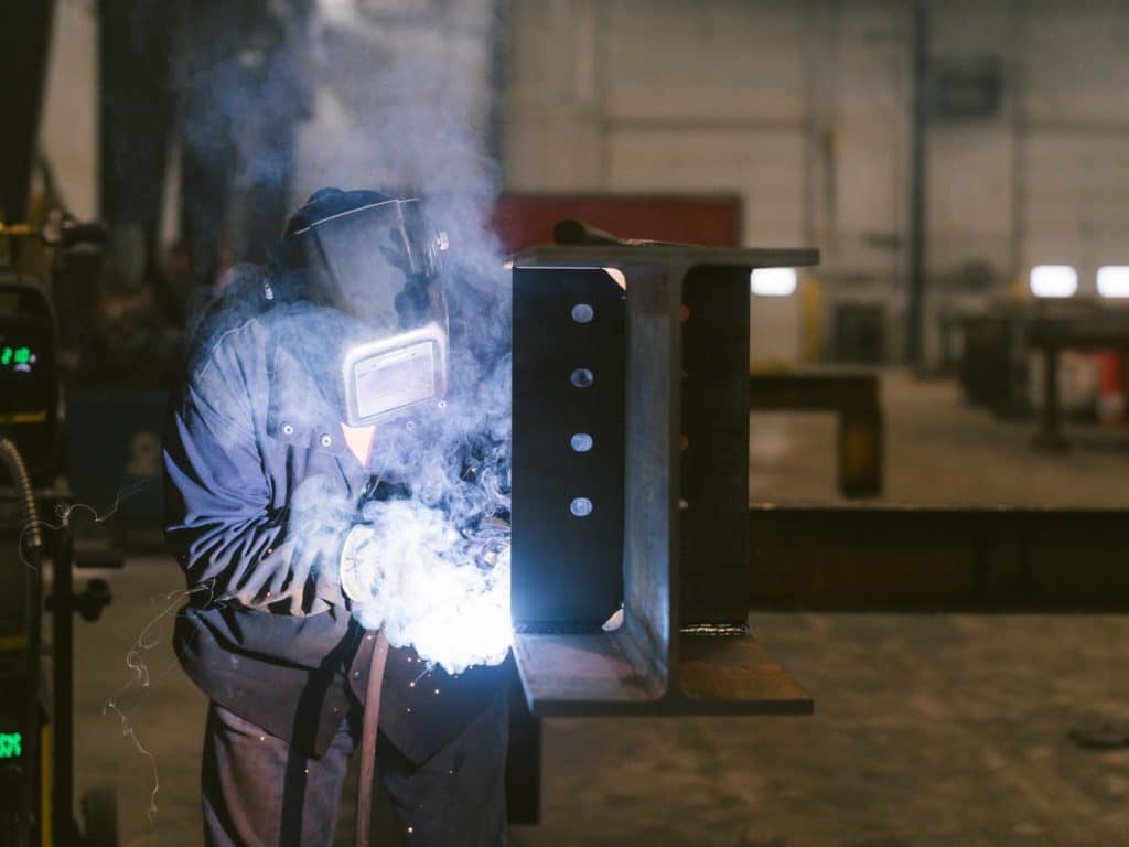 Person welding a metal beam in an industrial workshop.