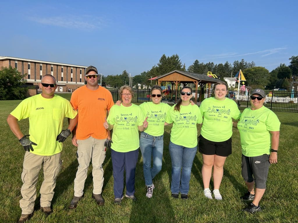 Group of volunteers in matching green shirts standing together on a grassy field.